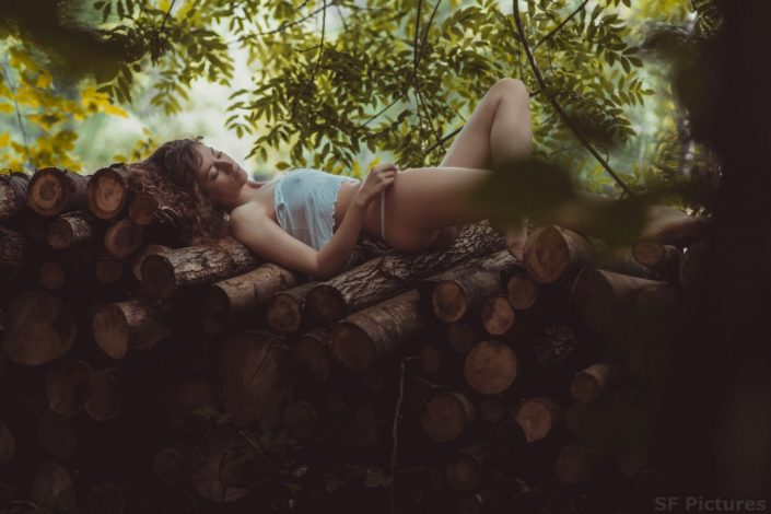 stunning brunette lying down on tree trunks with white top in the woods